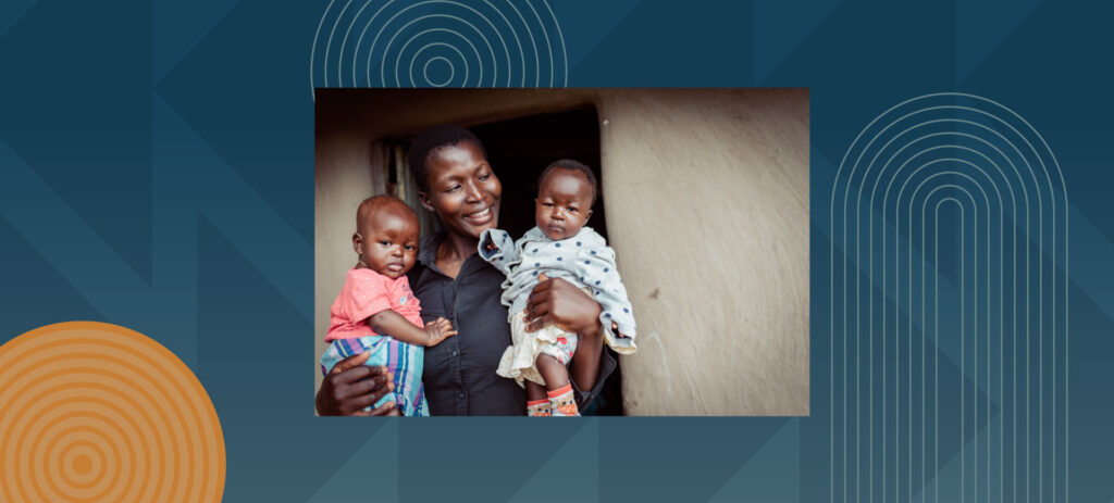 Smiling mother holding two young children in front of simple home entrance