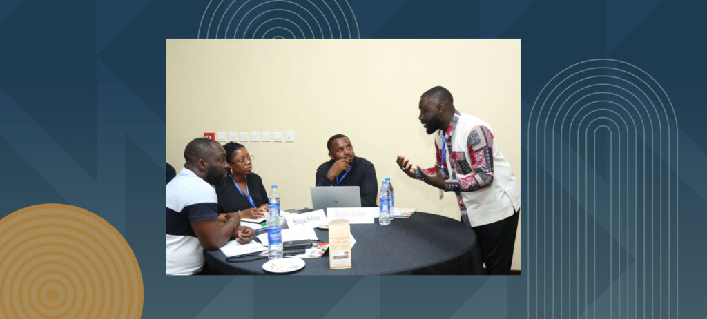 Business meeting with four professionals, one man standing presenting to three seated colleagues at conference table
